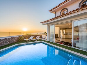 A modern pool area with a clear view of the sunset over the ocean, a stone wall, and two lounge chairs. - Luxury White Villa Sea View, Pool (Adeje)