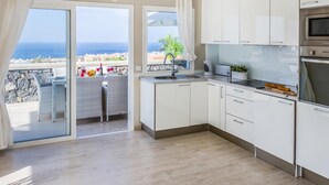 A modern kitchen with white cabinets, a built-in oven, and a view of the ocean through large windows. - Luxury White Villa Sea View, Pool (Adeje)