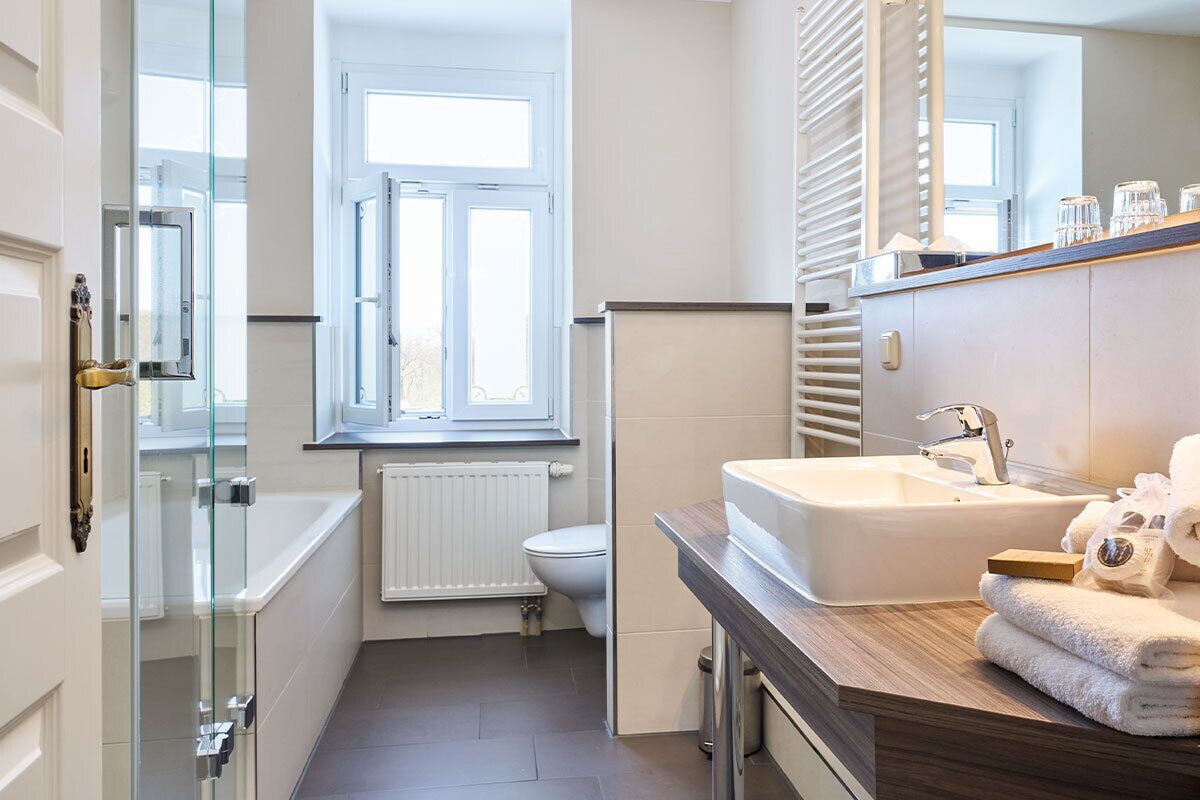 Une petite salle de bain dotée d’une douche à parois de verre, de toilettes blanches, d’une fenêtre et d’un lavabo avec un plan de travail en bois.