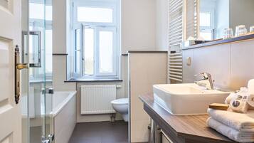 Une petite salle de bain dotée d’une douche à parois de verre, de toilettes blanches, d’une fenêtre et d’un lavabo avec un plan de travail en bois.