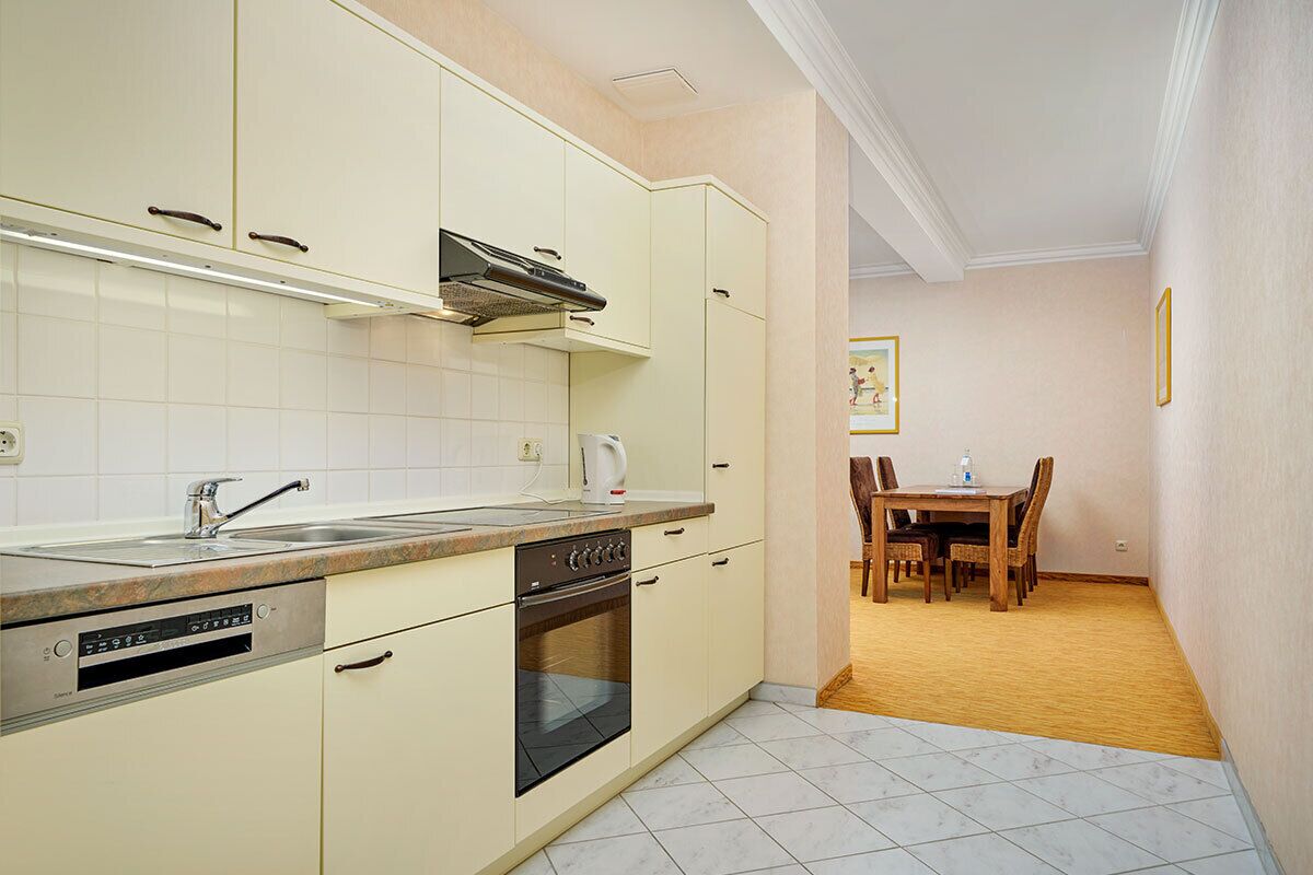 Una cocina con armarios blancos, una estufa y un lavamanos. Hay una zona de comedor con una mesa y sillas.