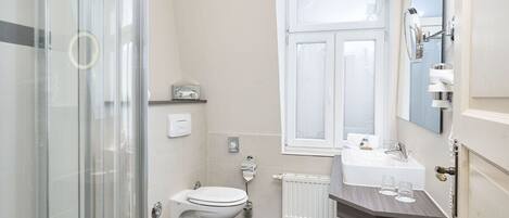 A modern bathroom with a glass shower enclosure, a white toilet, a sink with a mirror, and a window providing natural light.