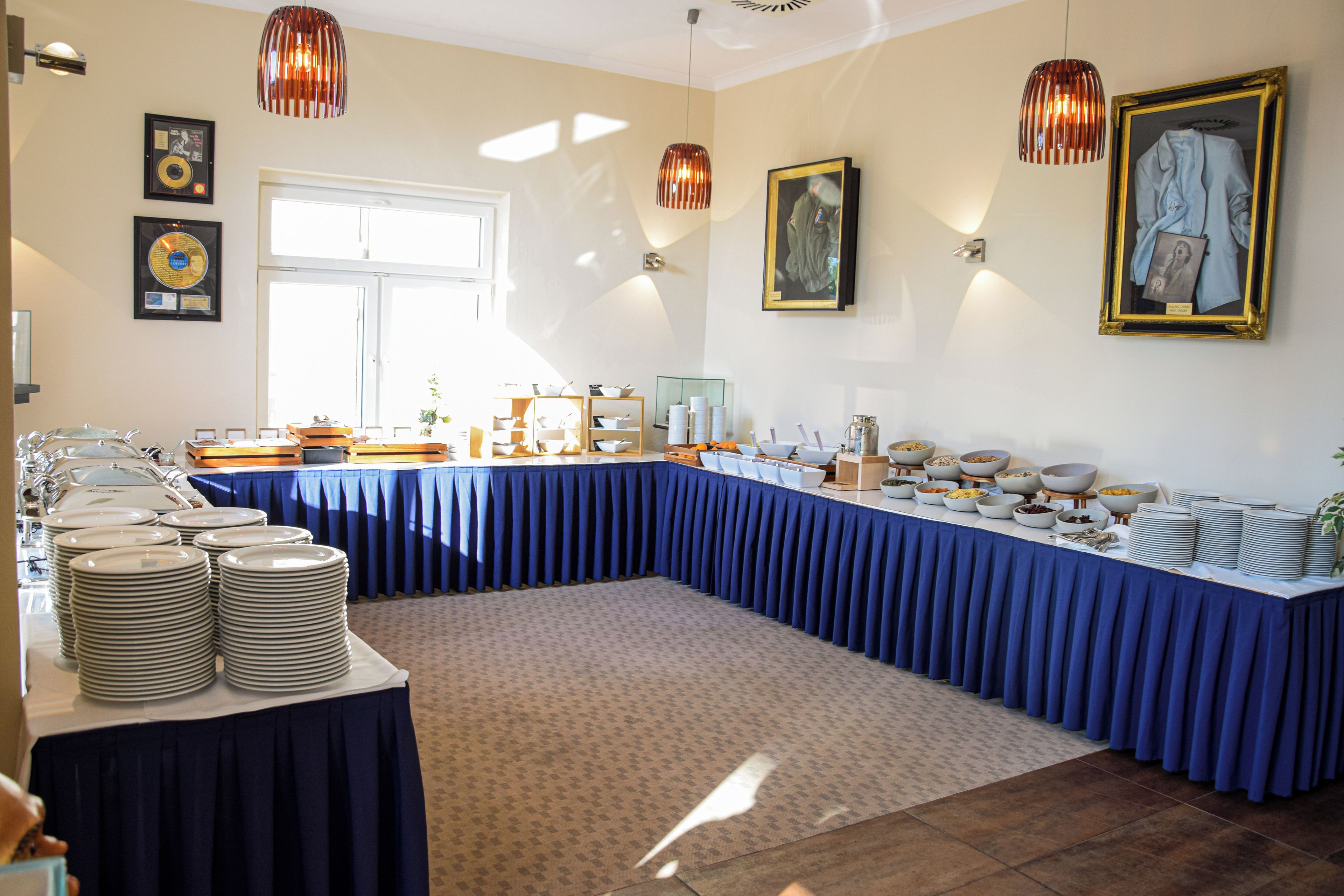 A buffet setup with a long table covered in blue, surrounded by stacks of white plates and bowls.