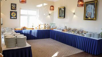 A buffet setup with a long table covered in blue, surrounded by stacks of white plates and bowls.