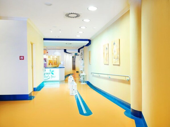 A hallway with a blue and yellow color scheme, white railings, and a reception area in the distance. -  Strand- und Wellnesshotel Preussenhof (Zinnowitz)