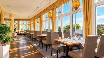 Ein Hotel-Speisesaal mit Tischen, Stühlen und großen Fenstern, die einen Blick ins Freie bieten.