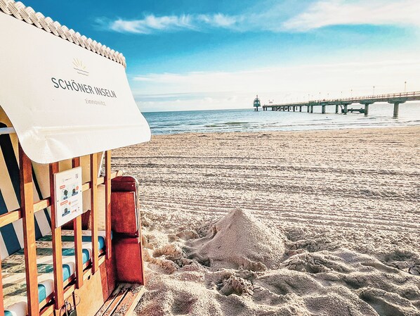 Una playa con una estructura de madera, un letrero con texto y un muelle al fondo.