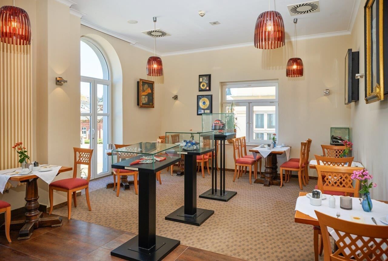 Un comedor con mesas y sillas de vidrio, un ventanal grande y lámparas colgantes decorativas.