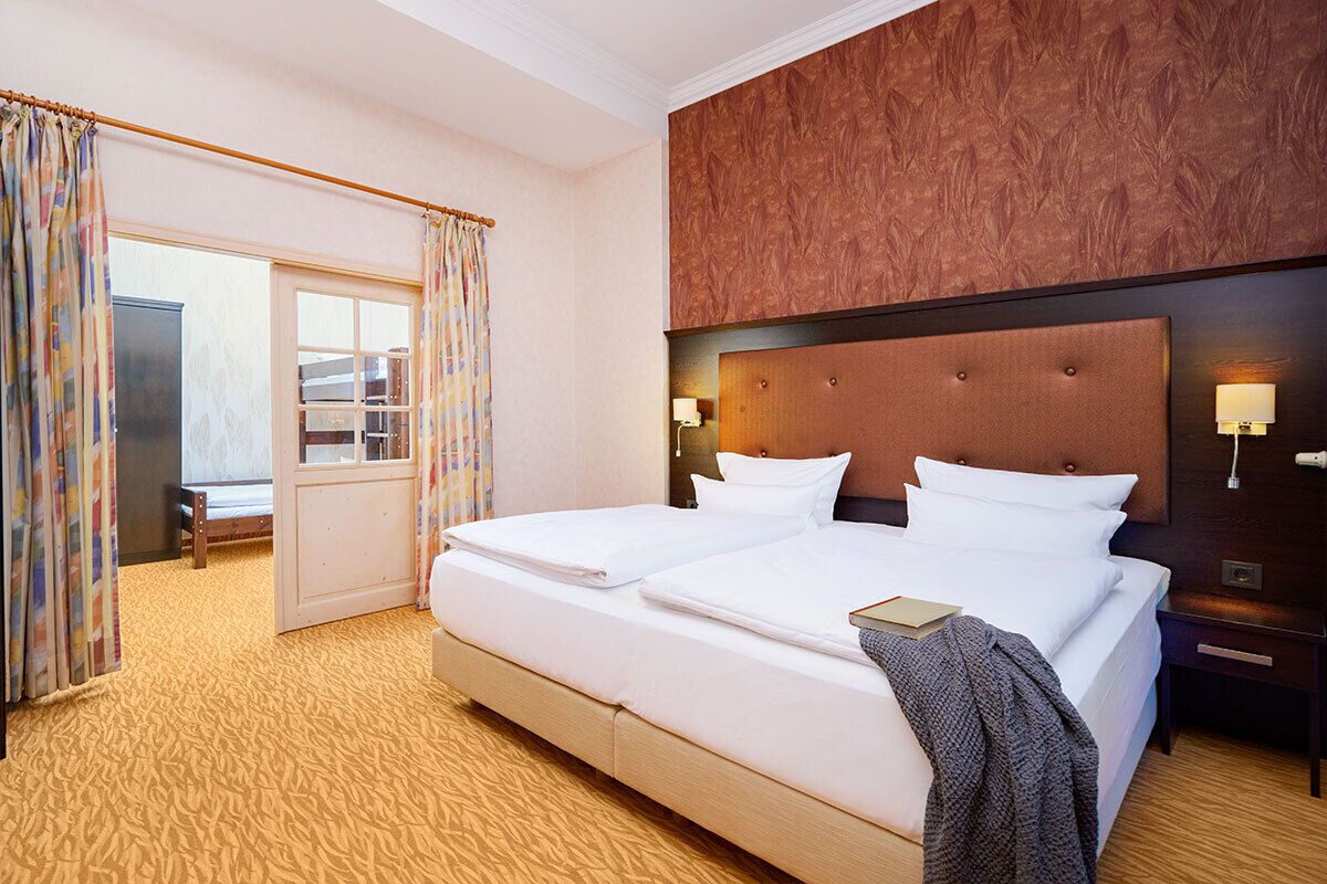 A hotel room with a large bed, a wooden headboard, two bedside tables with lamps, a window with curtains, and a view of the outside.