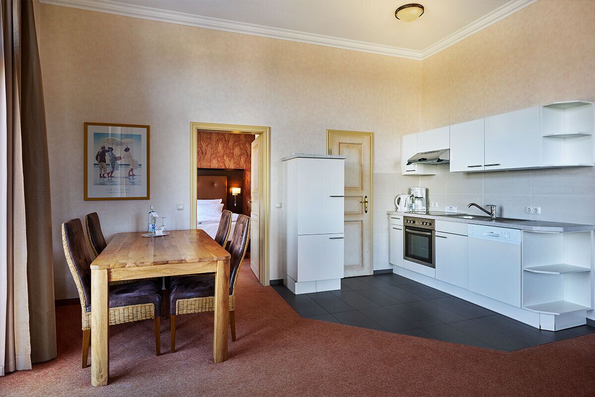 A compact kitchen with white cabinets, a built-in oven, and a dishwasher. There is a dining table with chairs in the adjacent room.