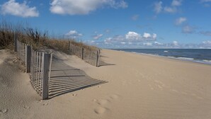 A sandy beach with a wooden fence and ocean waves in the background.