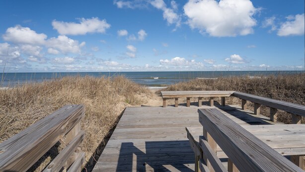 A wooden boardwalk leading to the beach with a clear view of the ocean and sky.