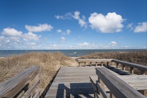 A wooden boardwalk leading to the beach with a clear view of the ocean and sky.