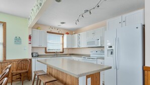 A kitchen with a central island, wooden chairs, a dining table, white cabinets, and a white refrigerator.