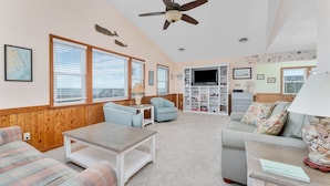 A cozy living room with a wooden paneled wall, a ceiling fan, a television, and a bookshelf.