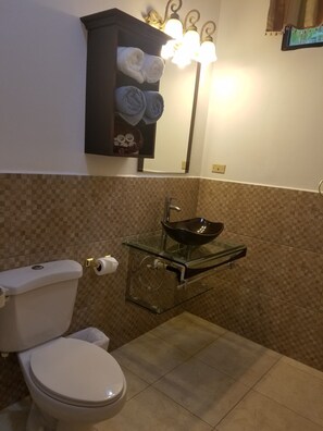 A bathroom with a toilet, a glass sink with a black basin, and a towel rack with towels. - Hotel Club Quinta Pat Resort & Restaurant (San Antonio de Oriente)