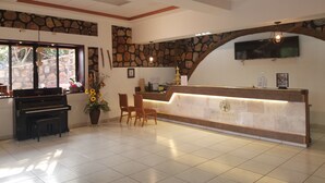 A hotel reception area with a piano, a reception desk, and a stone wall. - Hotel Club Quinta Pat Resort & Restaurant (San Antonio de Oriente)