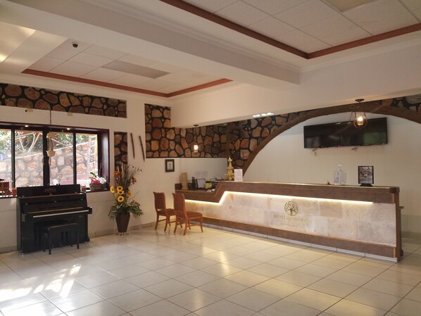 A hotel reception area with a piano, a reception desk, and a stone wall. - Hotel Club Quinta Pat Resort & Restaurant (San Antonio de Oriente)