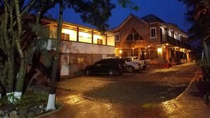 A two-story building with a brick facade and a balcony. There are cars parked in front and a paved driveway. - Hotel Club Quinta Pat Resort & Restaurant (San Antonio de Oriente)