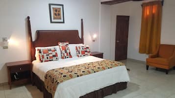 Un dormitorio ordenado con una cama grande, cabecera de madera, mesita de noche, una silla y una puerta.