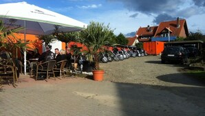Un espacio al aire libre con mesas y sillas, una fila de motocicletas estacionadas y un edificio con techo rojo al fondo.