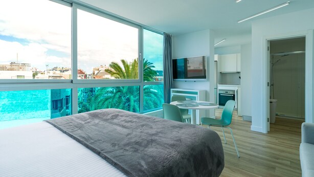 Ein modernes Hotelzimmer mit einem großen Bett, einem Balkon mit Blick auf die Stadt, einem Essbereich und einer Küchenzeile.