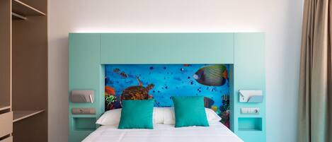 A hotel room with a bed, teal pillows, a mural of underwater scene, and a wooden wardrobe.
