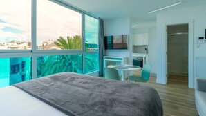 Ein modernes Hotelzimmer mit großem Fenster, einem Bett, einem Essbereich und einer Küchenzeile.
