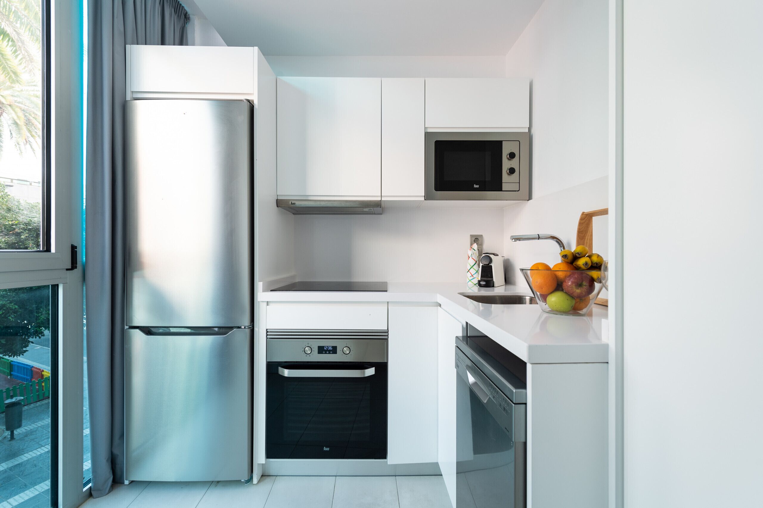 A modern kitchen with stainless steel appliances, white cabinetry, and a fruit bowl on the counter.