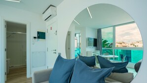 Ein modernes Hotelzimmer mit Sofa, Fernseher, Schreibtisch und einem großen Fenster mit Blick auf die Stadt.