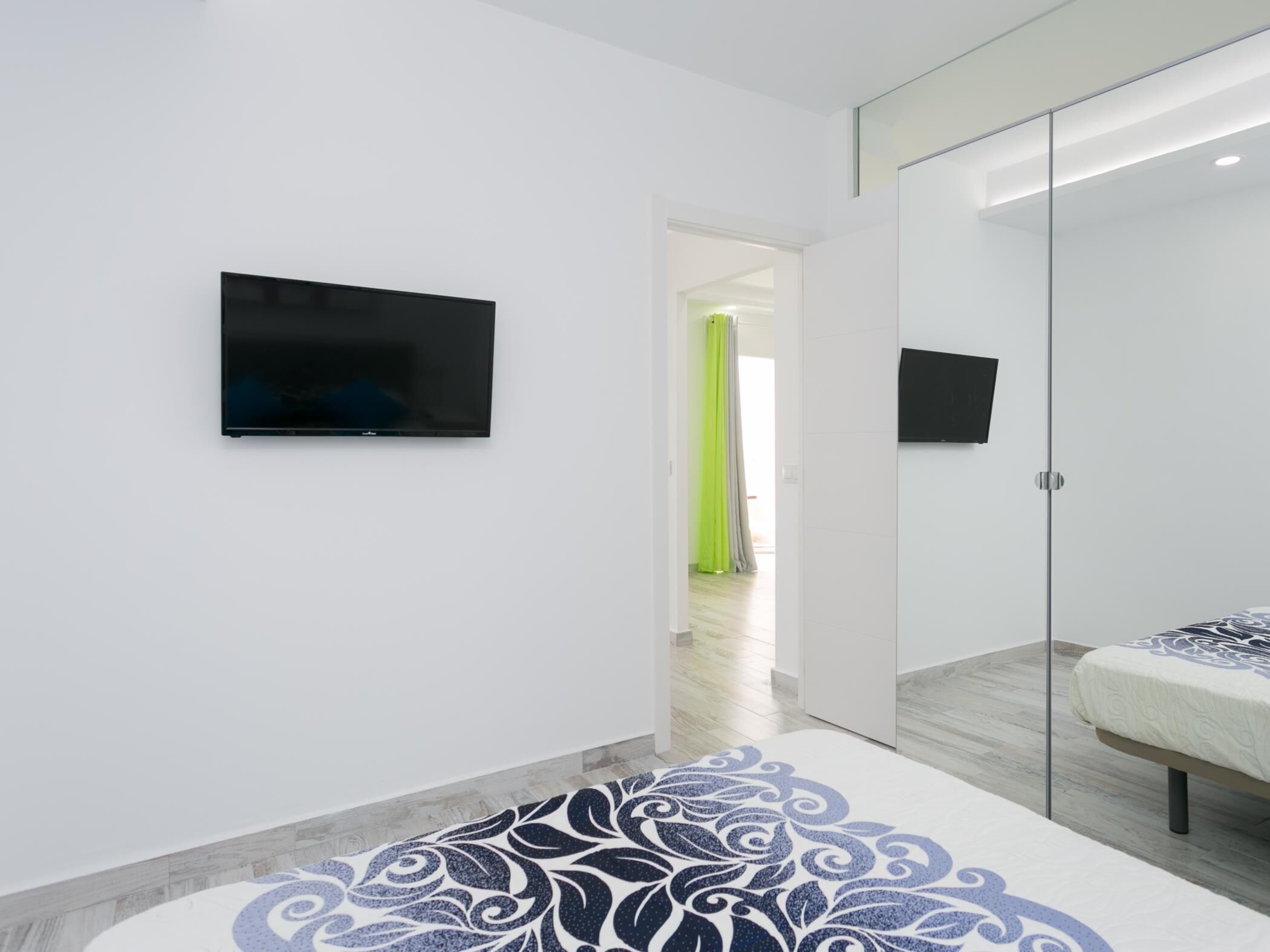 A modern bedroom with a bed, a television mounted on the wall, and a mirror.