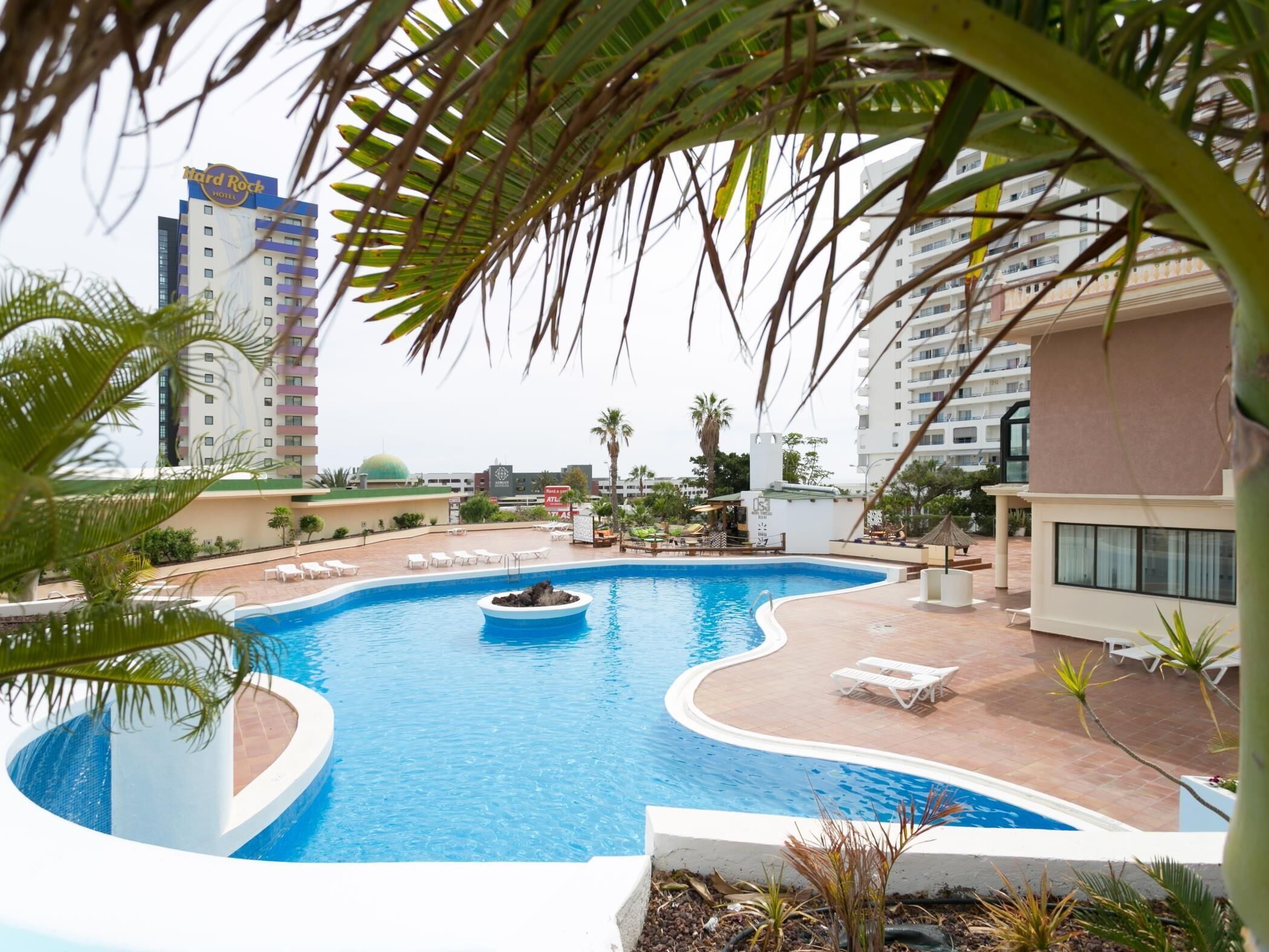 A hotel pool area with a circular water feature, lounge chairs, and palm trees.