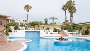 A swimming pool with a waterfall feature, surrounded by palm trees and lounge chairs.