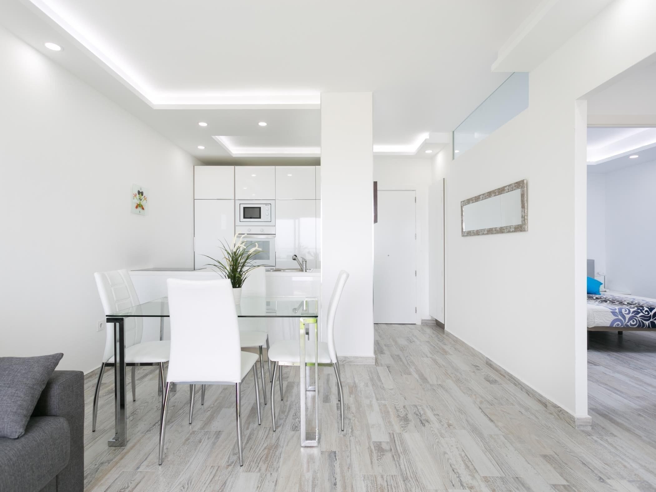 Un ambiente living moderno e minimalista con un tavolo da pranzo in vetro, sedie bianche e un divano grigio.