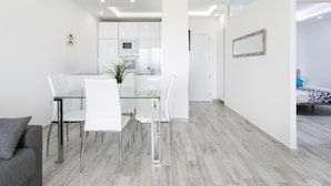 A modern, minimalist living space with a glass dining table, white chairs, and a grey sofa.