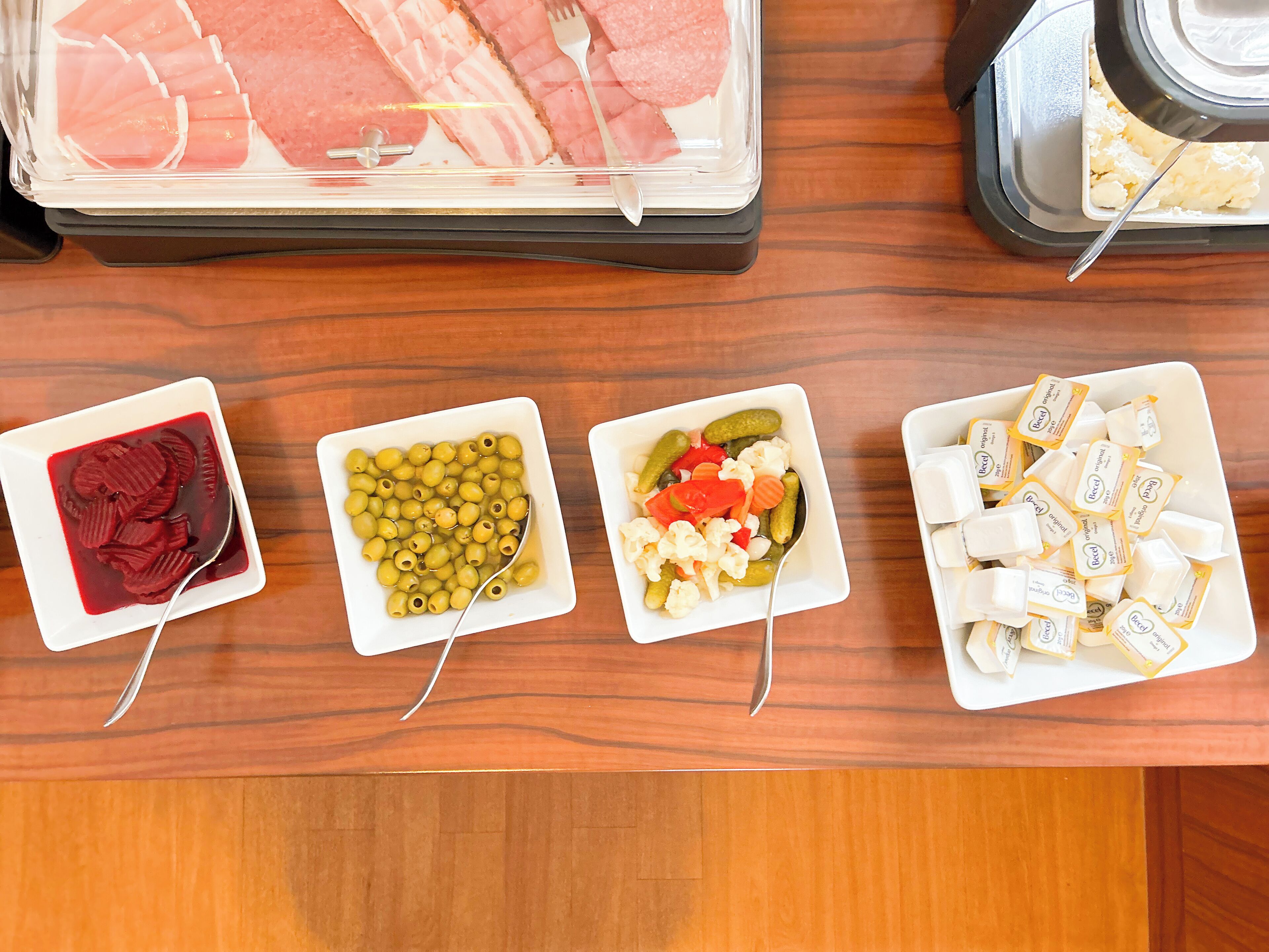 A buffet table with various food items including sliced meats, olives, pickled vegetables, and cheese.