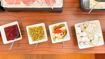 A buffet table with various food items including sliced meats, olives, pickled vegetables, and cheese.