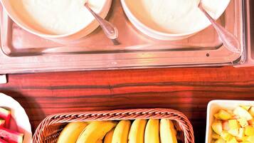 Une table de buffet avec des plats contenant des aliments blancs, un panier de bananes et un saladier de fruits coupés en dés.