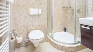 Un baño moderno con inodoro, ducha con mampara de vidrio y lavamanos blanco.