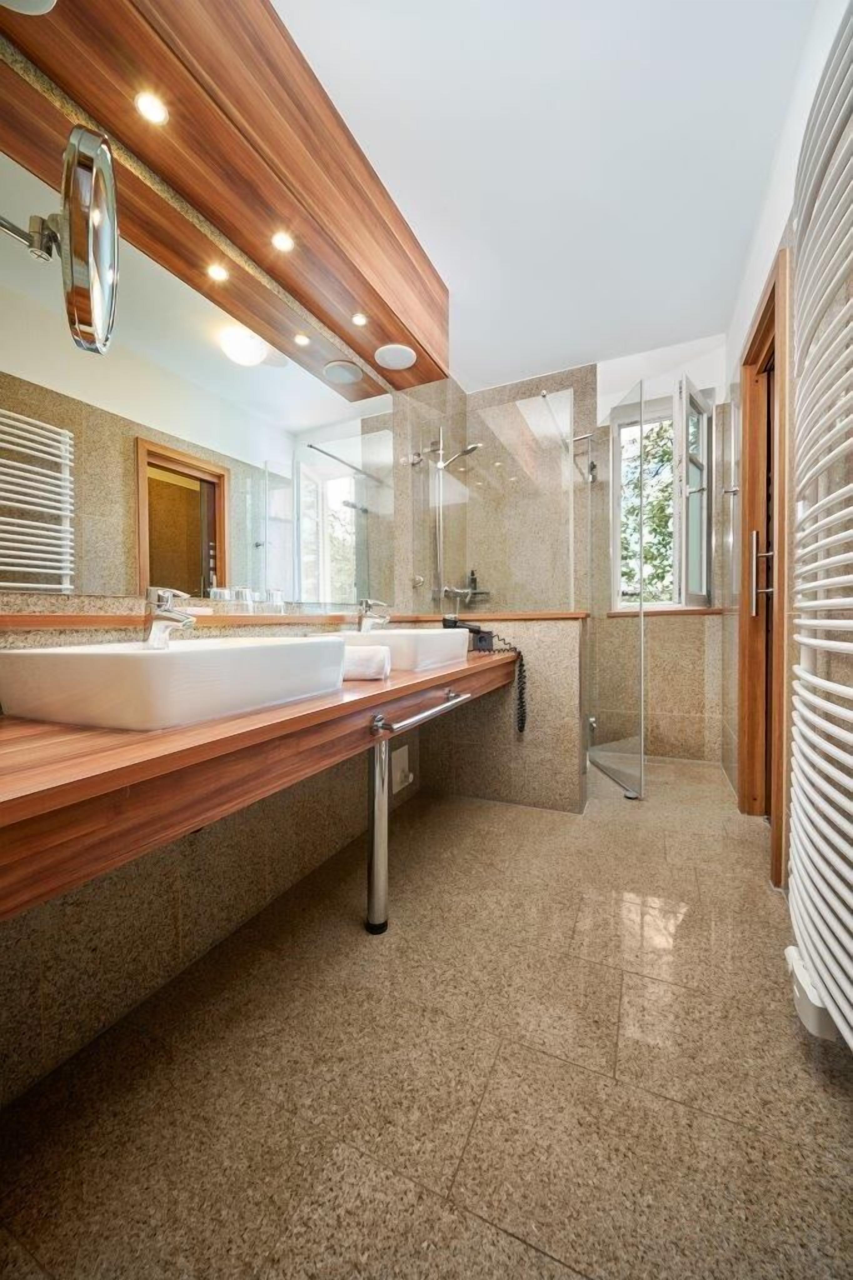 Un bagno moderno con un mobile bagno in legno, due lavabi, cabina doccia in vetro e uno specchio grande.