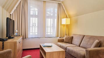 A hotel room with a sofa, a wooden coffee table, a television, and a lamp.