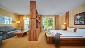 Ein Hotelzimmer mit Bett, einer Couch, einem Holztisch und einem Balkon mit Blick auf Grünflächen.