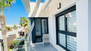 Ein moderner Balkon mit Glasgeländer, einem Sessel und Blick auf die Umgebung, inklusive Pool und Palmen.
