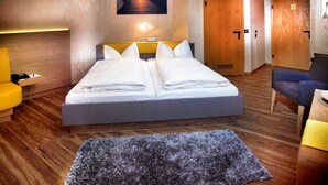 Een hotelkamer met een tweepersoonsbed, een klein bureau met stoel, een bank en een groot vloerkleed op de houten vloer.