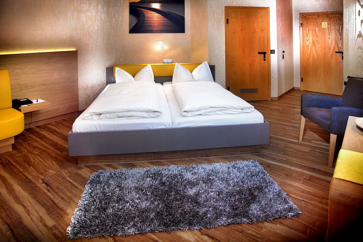 Une chambre d’hôtel avec un lit double, un petit bureau avec une chaise, un canapé et un grand tapis sur le plancher en bois.