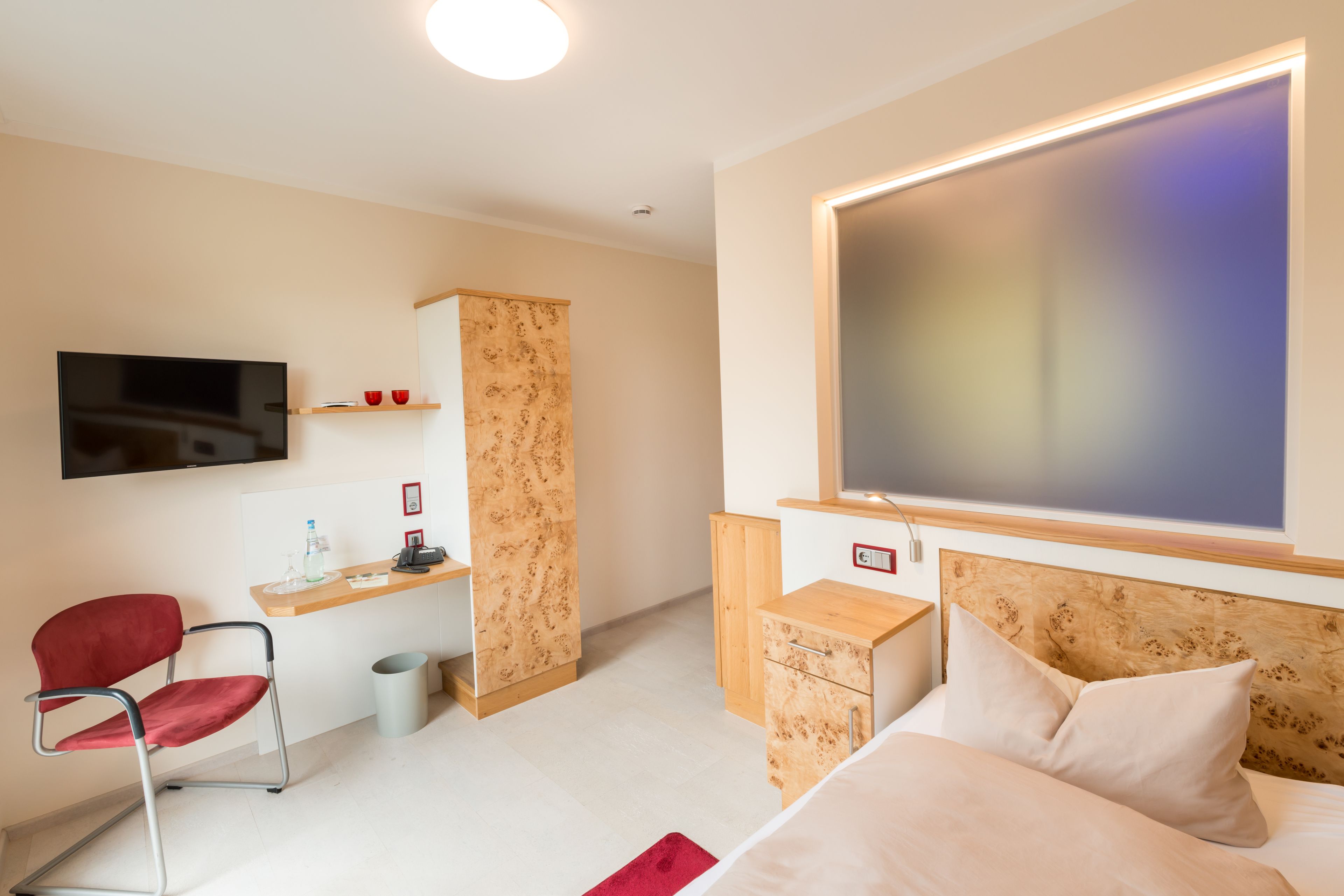 A modern hotel room with a bed, a desk, a chair, a TV, and a large window.