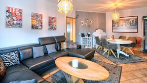 Ett modernt vardagsrum med en svart lädersoffa, ett träbord och en matplats med ett vitt bord och stolar.