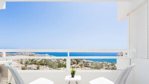 A balcony with two white wicker chairs, a small table with a plant, and a view of the sea and cityscape. - 1107 Sea view super Playa Las Americas (Playa de las Américas)
