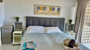 Une chambre d’hôtel bien aménagée, avec un grand lit, deux tables de chevet, une tête de lit, une œuvre d’art murale et une fenêtre avec des rideaux.