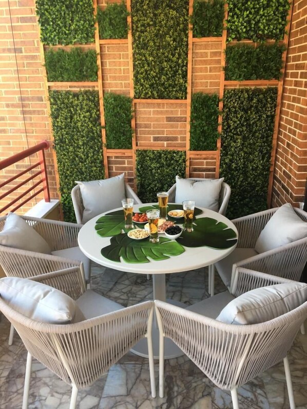 Une table ronde entourée de chaises blanches et agrémentée d’un set de table vert en forme de feuille, le tout adossé à un mur de briques orné de panneaux de verdure verticale.